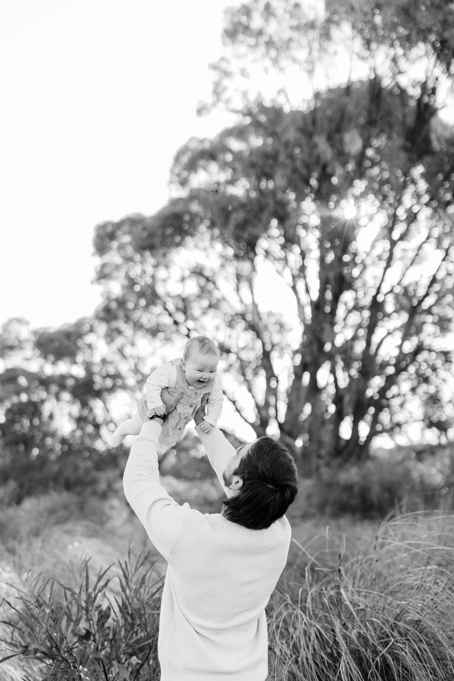 Child in white sweater reaching up towards sky in black and white nature scene.