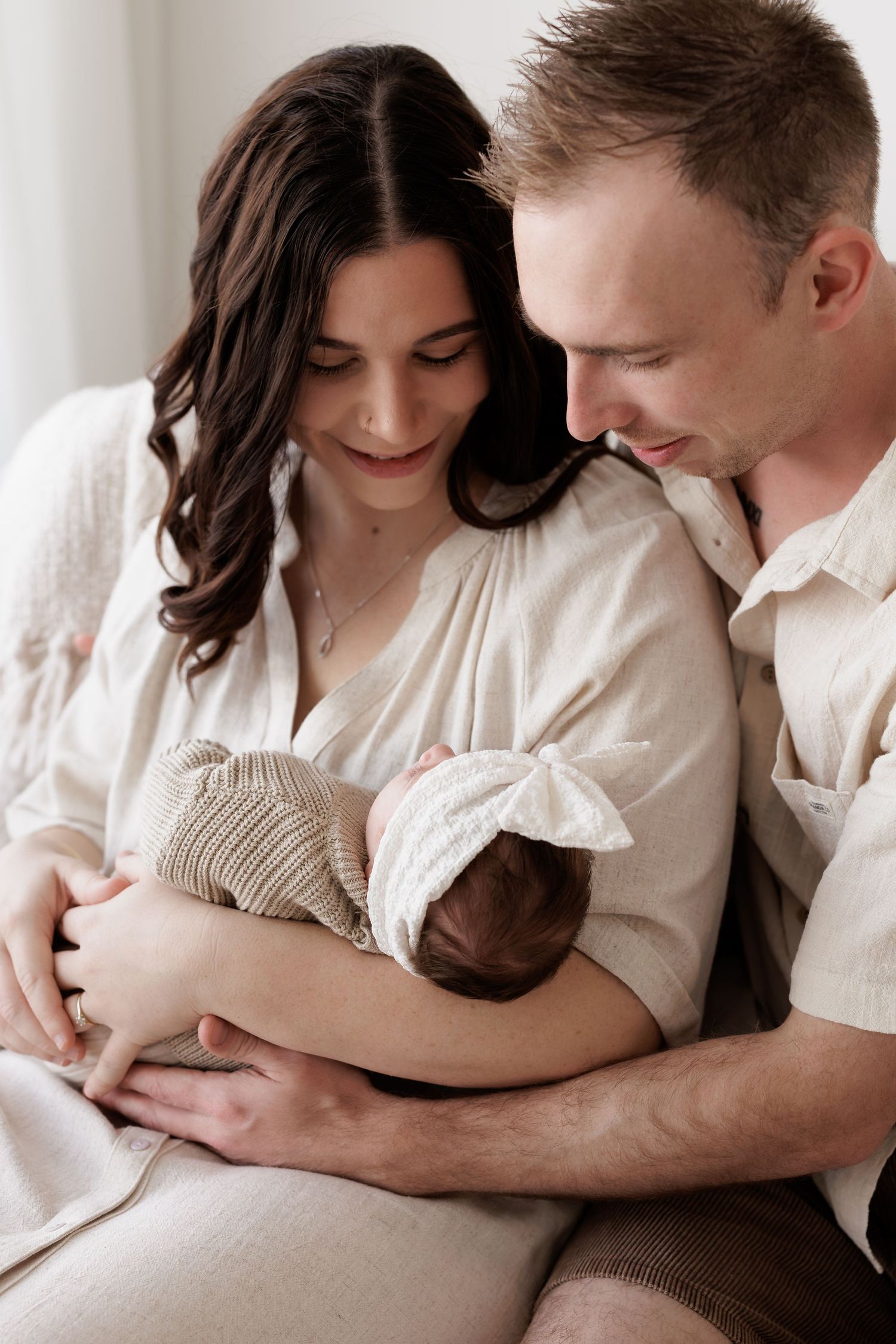 A couple shares an intimate moment with their newborn baby in soft lighting.