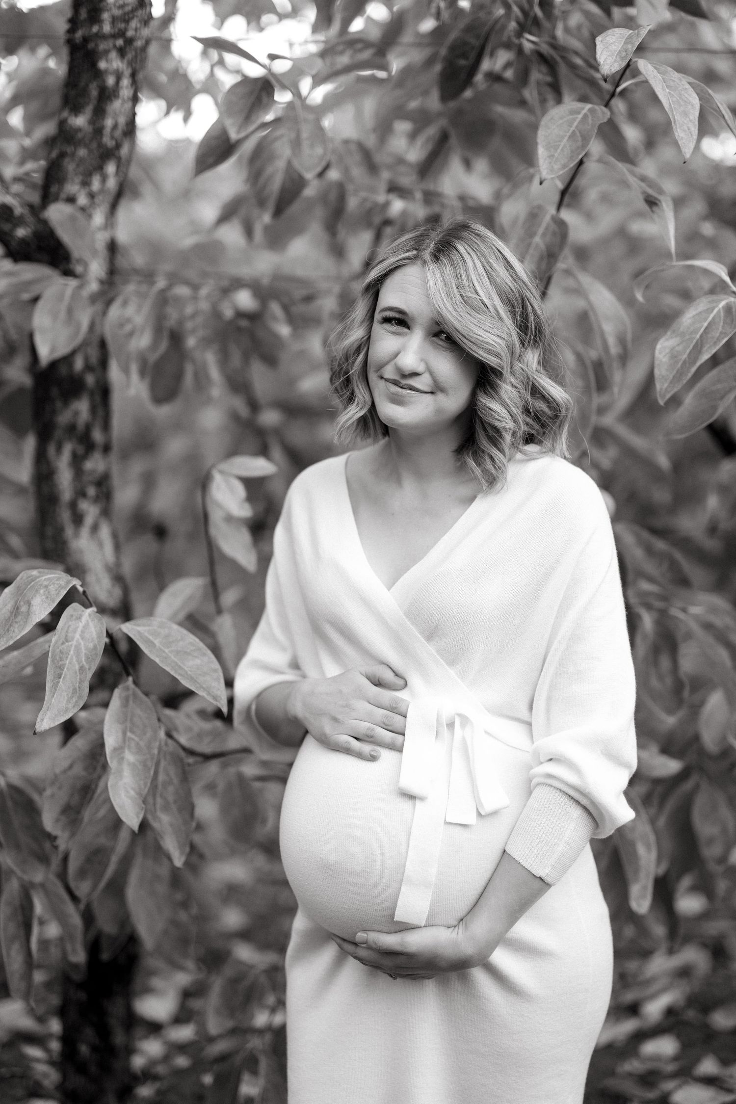 Black and white maternity portrait surrounded by leaves and branches.