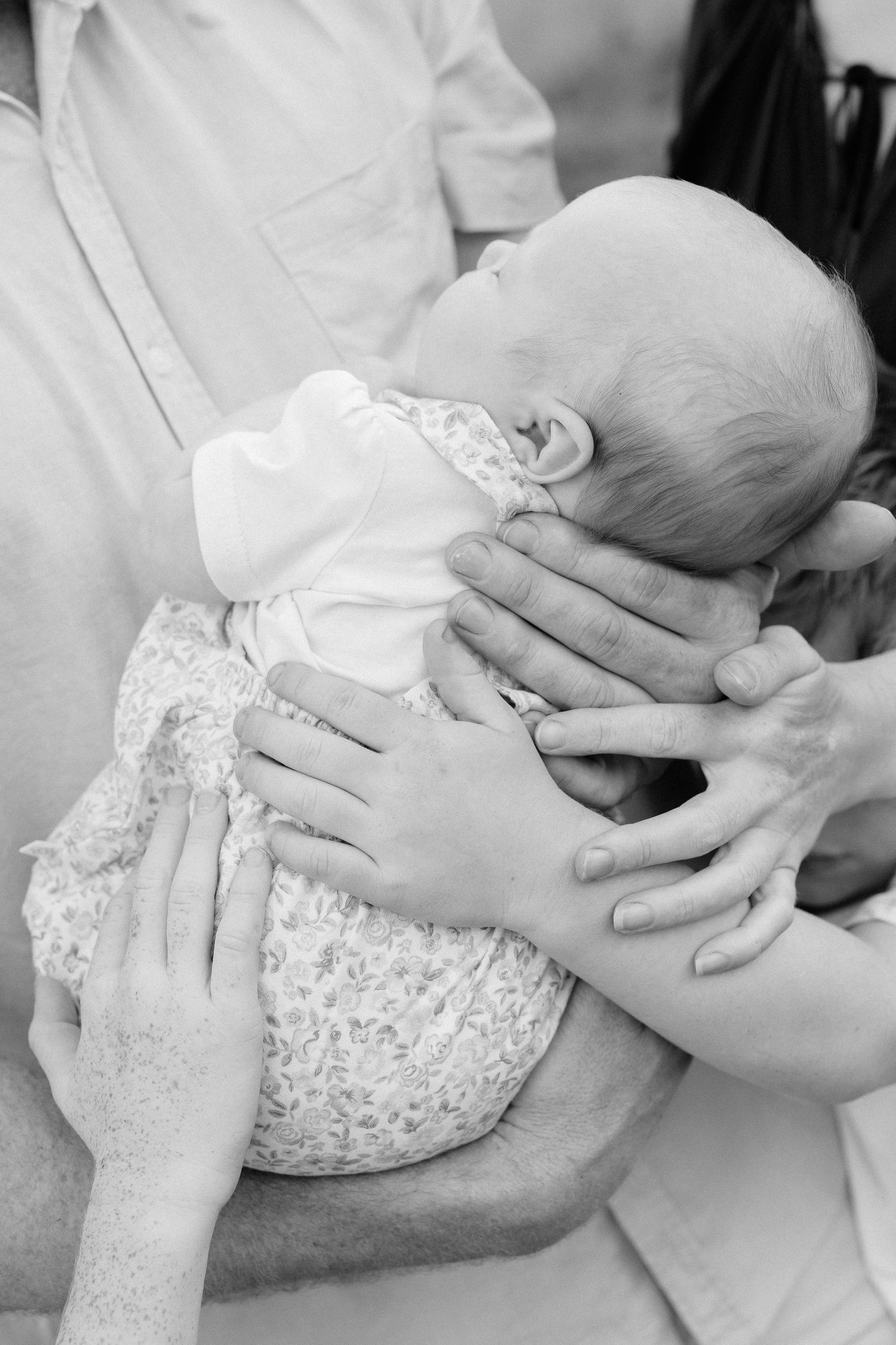 Close-up black and white photo of gentle hands cradling an infant.