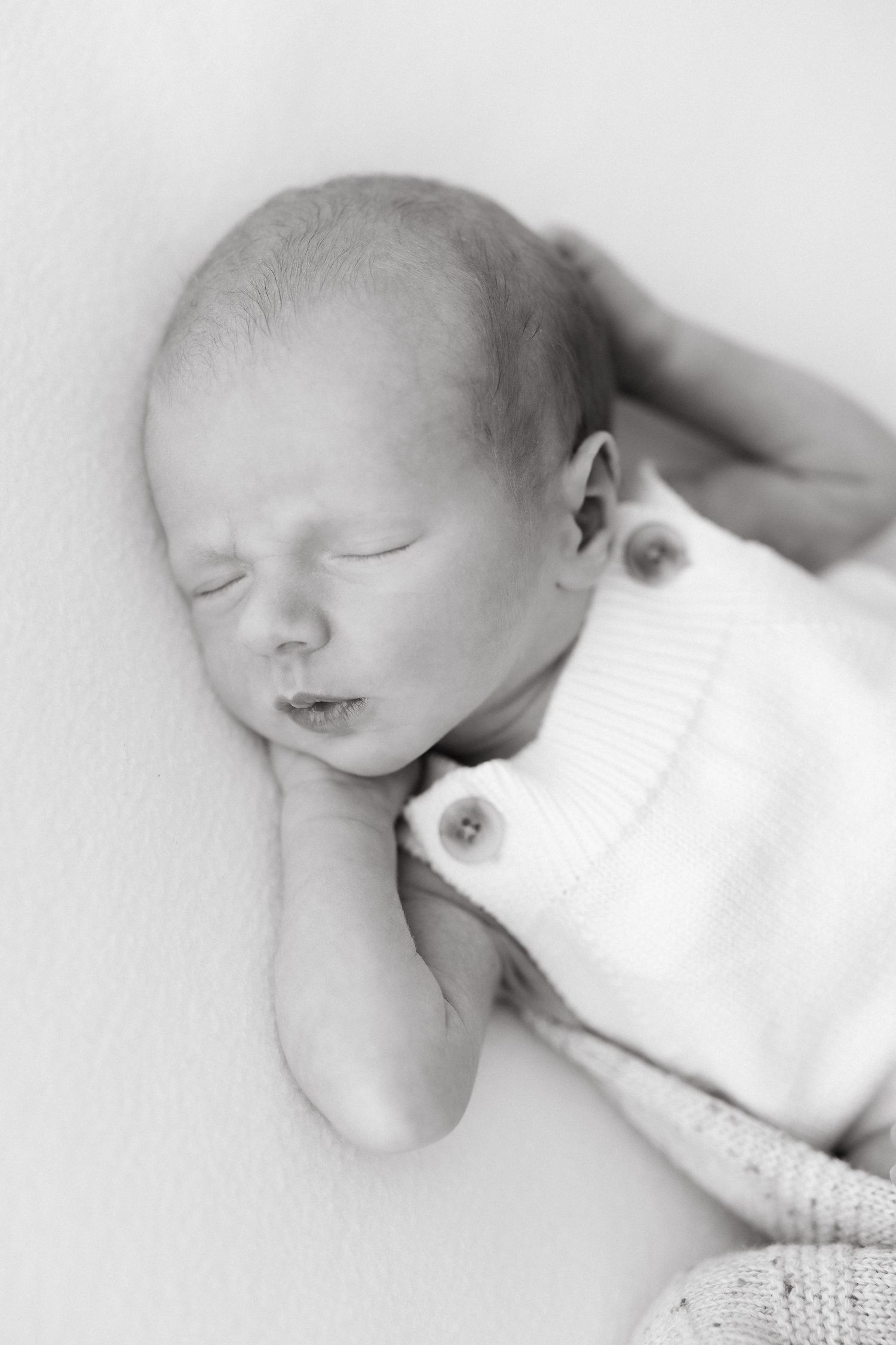 Peaceful sleeping newborn in white clothing against light background.