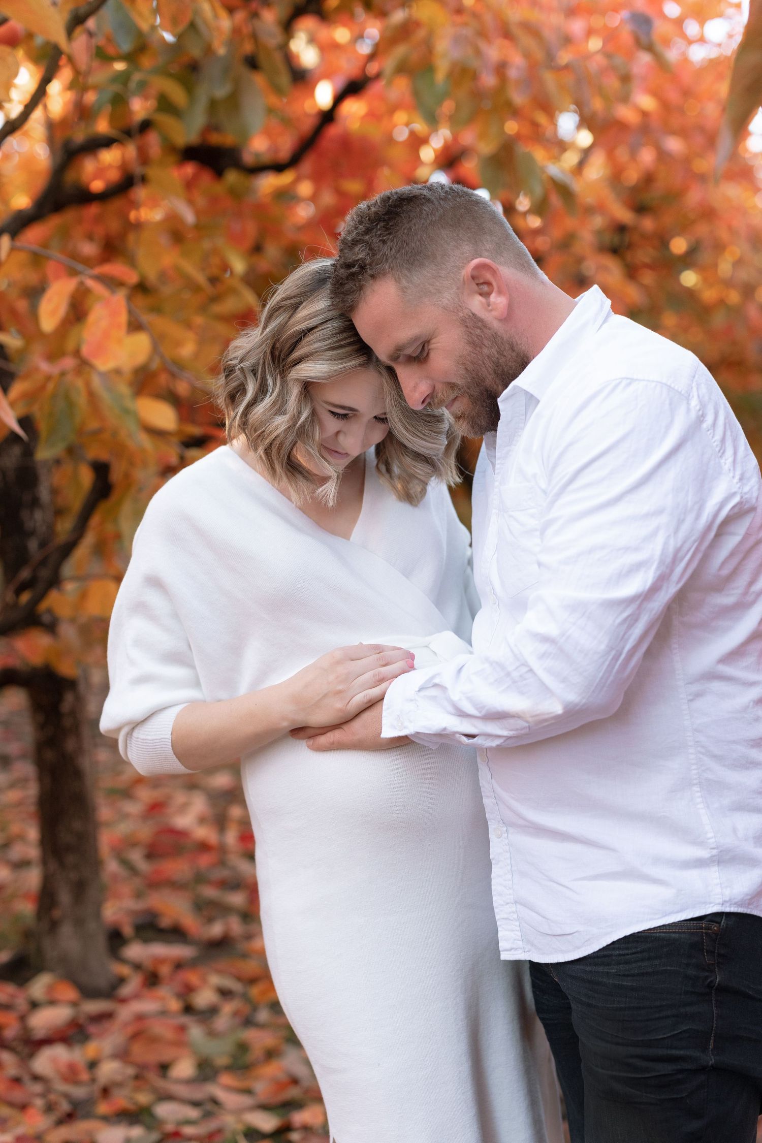 Intimate maternity photo beneath orange autumn trees.