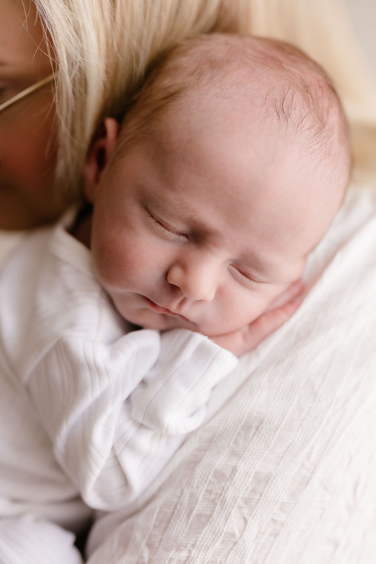 Peaceful sleeping newborn in white clothing against soft white bedding.