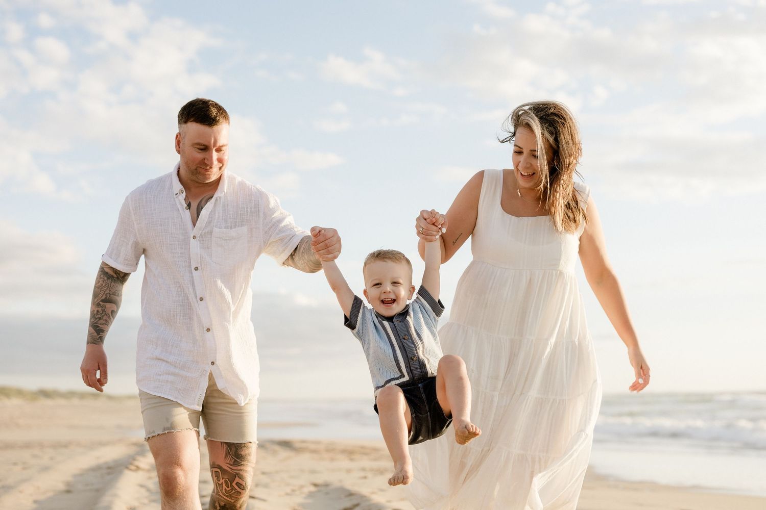 A family swings a small child between them while walking on a beach at sunset.