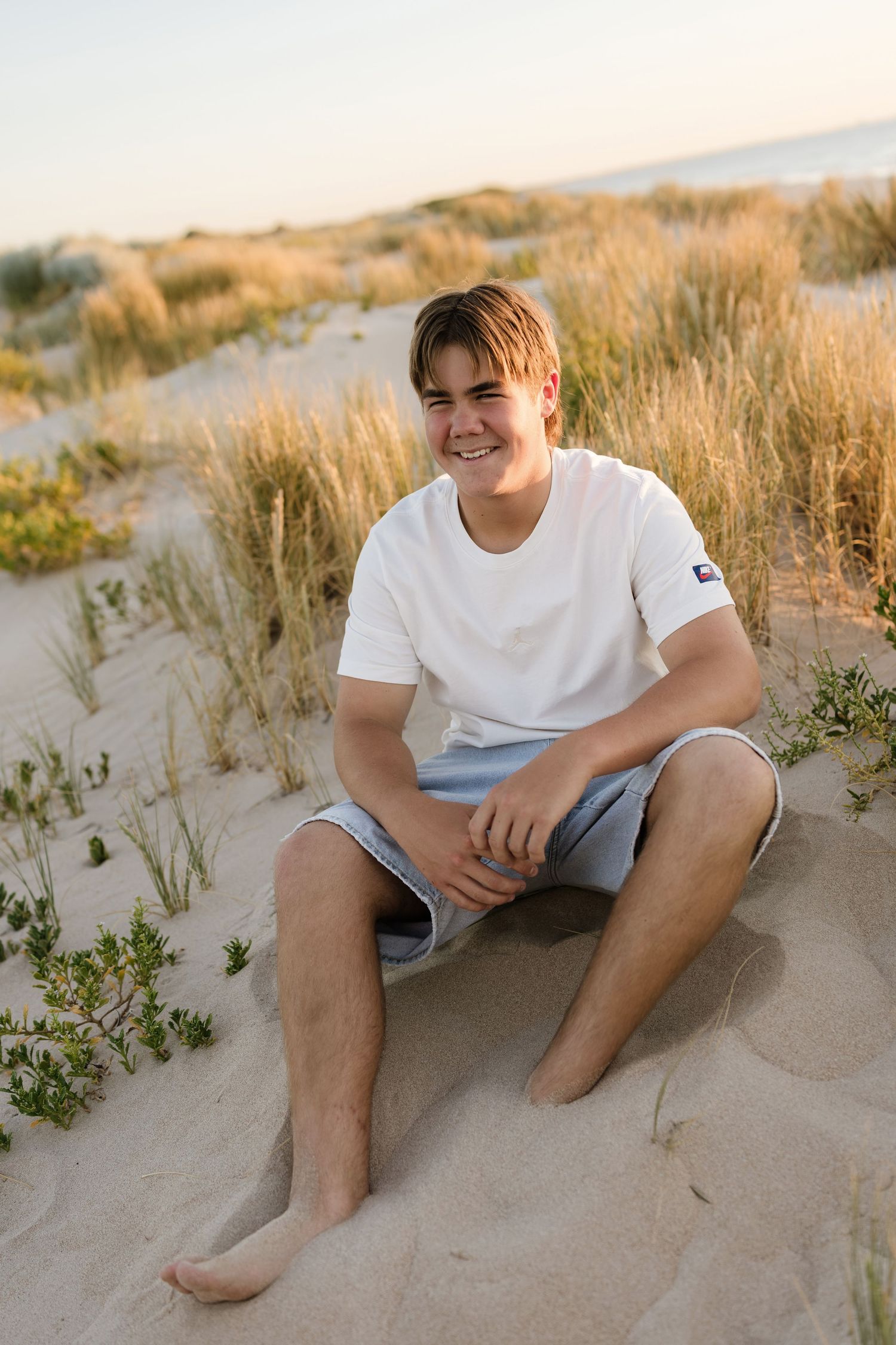 Candid portrait of someone sitting and laughing in beach sand dunes.