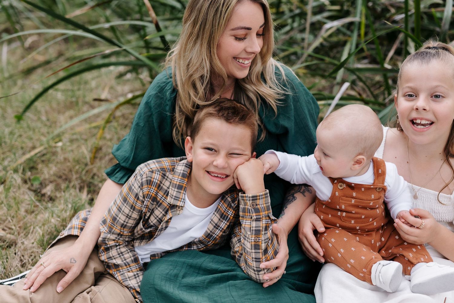 Family laughing together while sitting on blanket in natural outdoor setting.