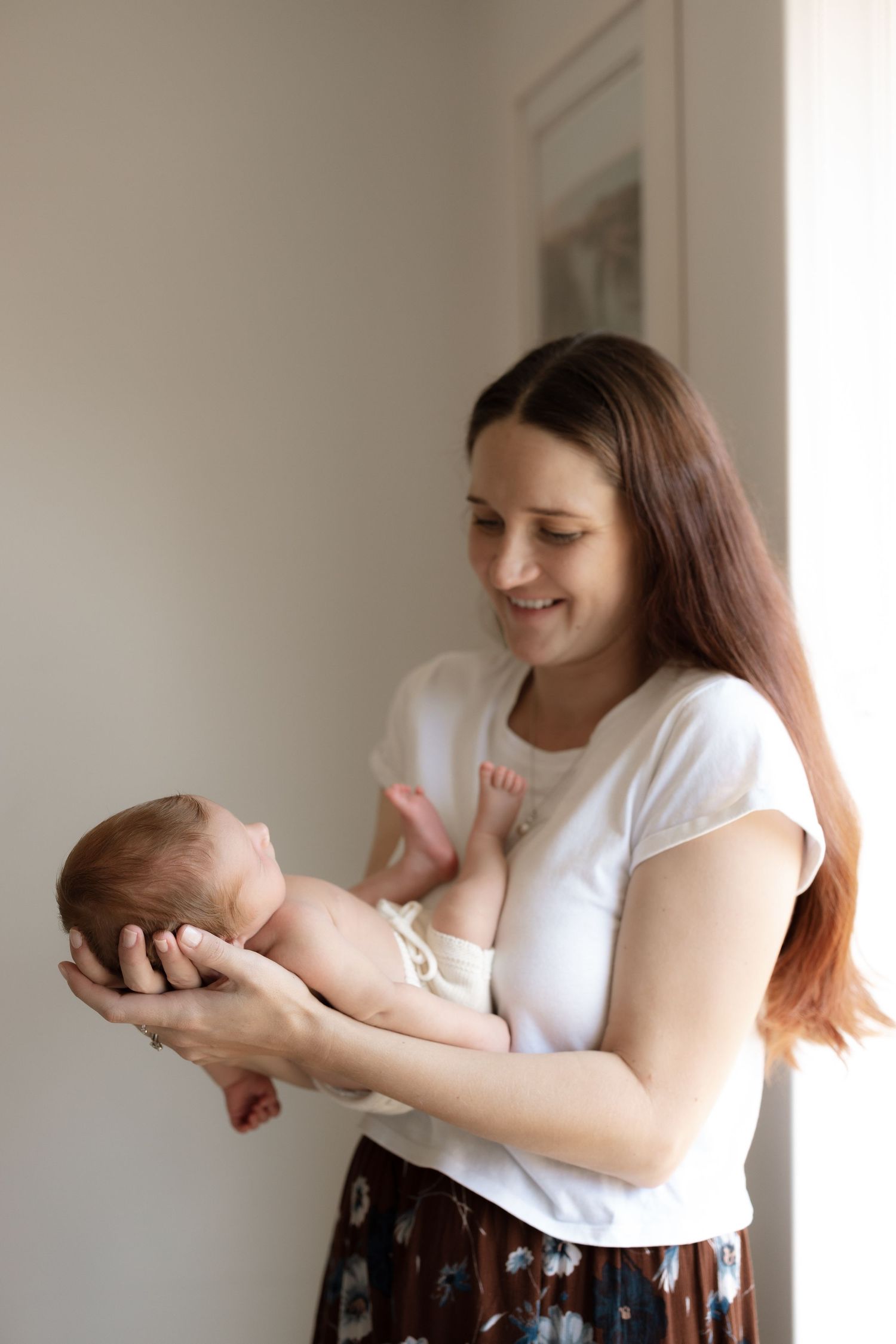 Joyful moment as parent cradles newborn baby against white wall background.