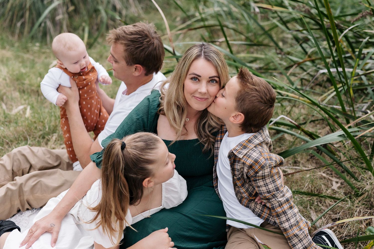 Candid outdoor family portrait with green reeds and natural lighting.