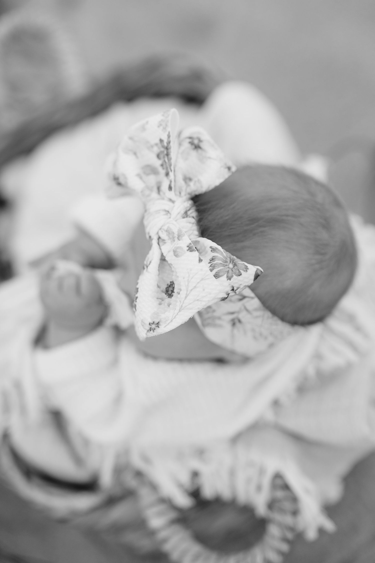 Close-up black and white photo of sleeping baby with delicate bow headband.