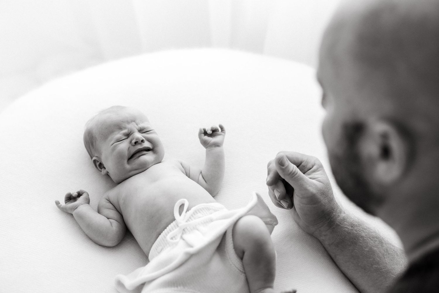 Candid moment of interaction with crying infant on white surface.