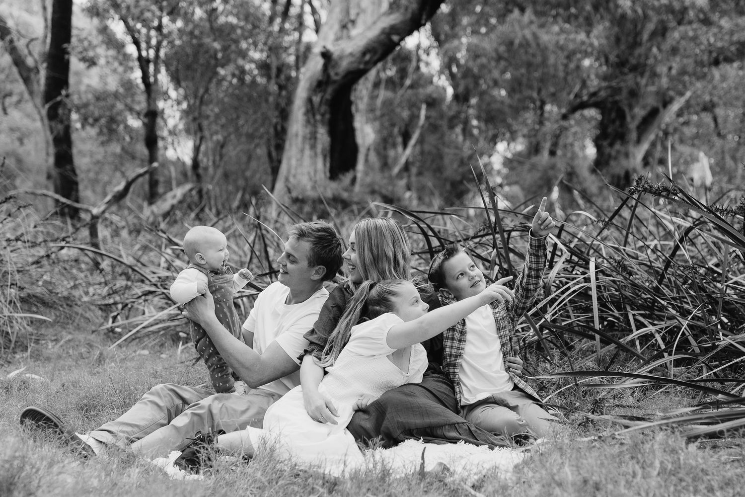 Black and white image of family relaxing together on ground near fallen branches.