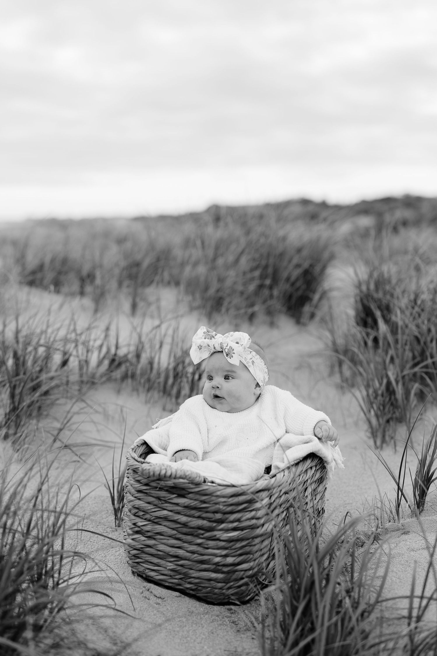 Infant resting in rustic basket among beach grass in black and white.