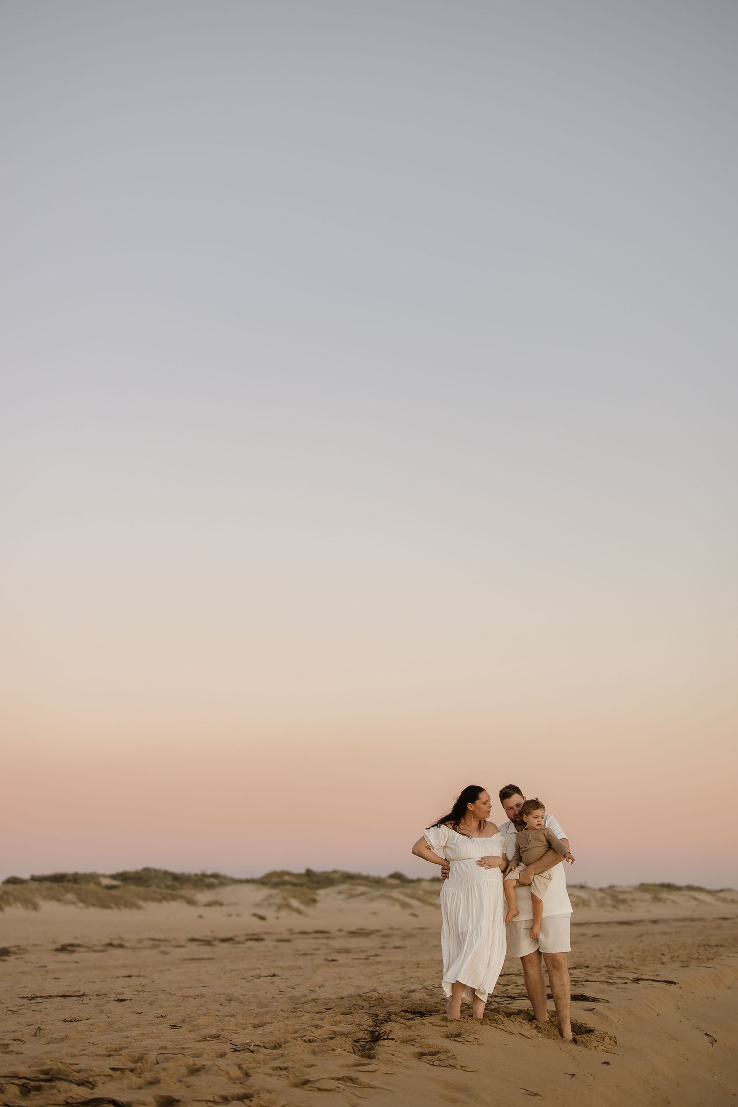 Family enjoying a playful moment together on sand dunes at sunset.