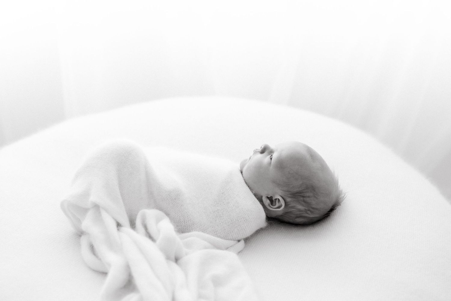 Newborn baby sleeping peacefully on white bedding in soft black and white tones.