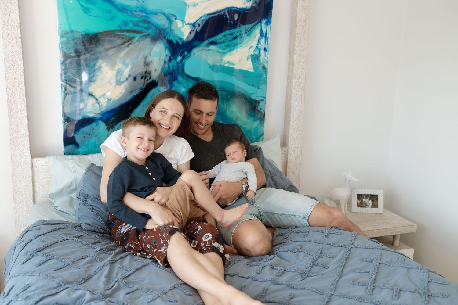 Family lounging together on gray bedding against vibrant blue wall art.