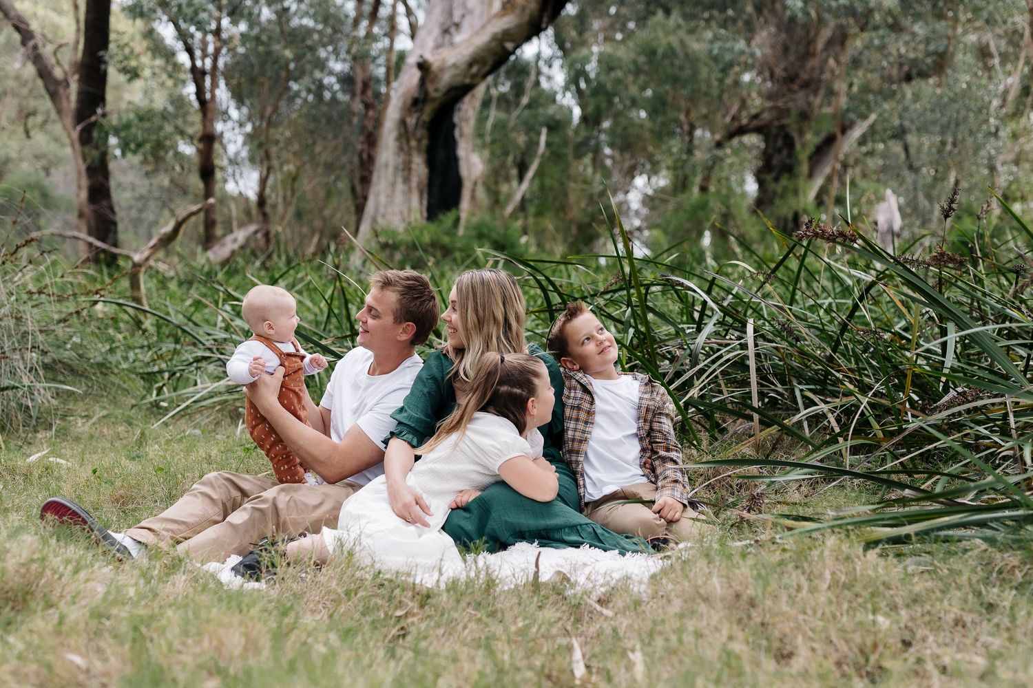 A relaxed family picnic scene in a natural wooded setting with everyone sitting on blankets.