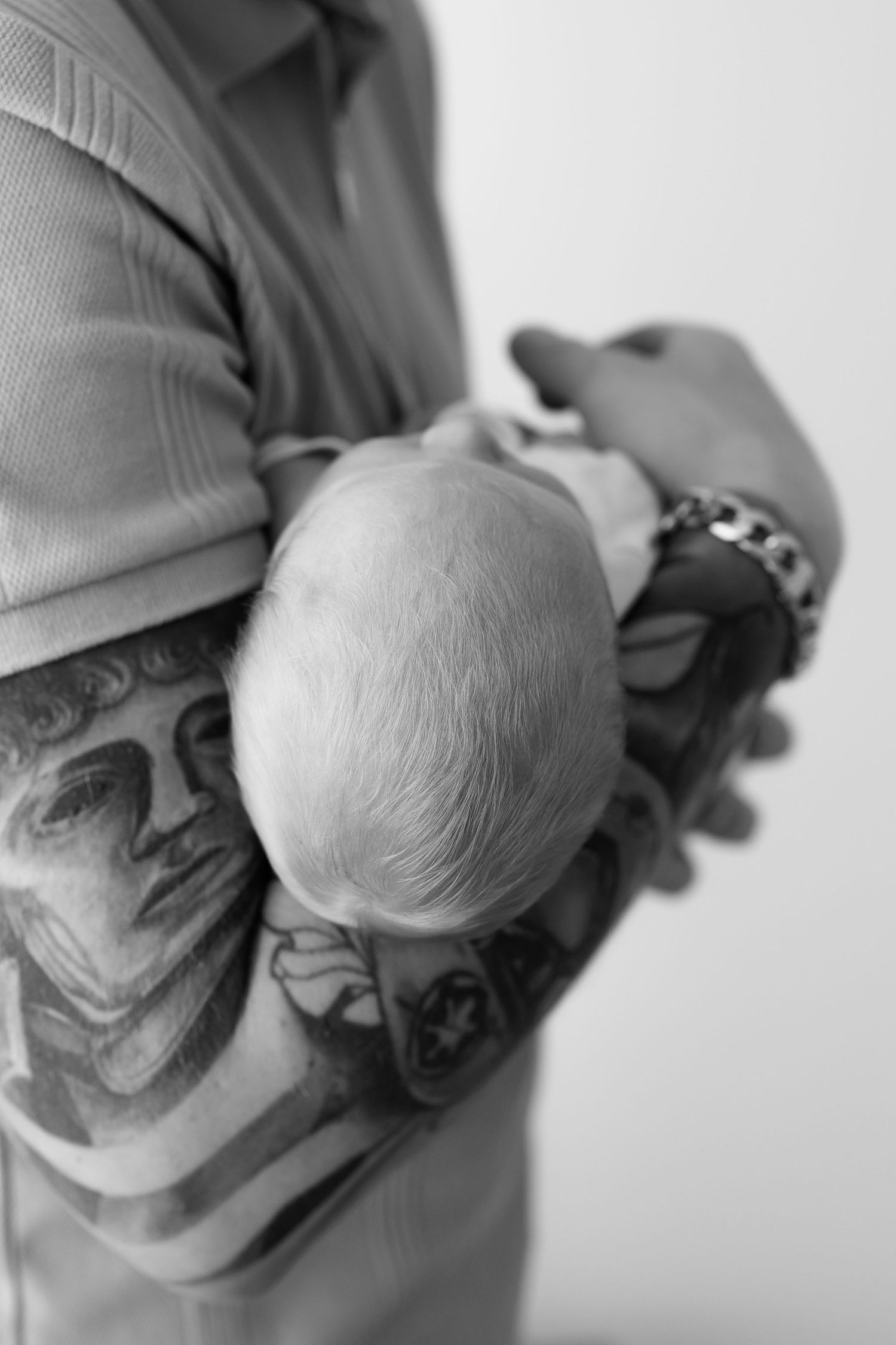 Close-up black and white photos of tattooed arms holding a newborn baby.