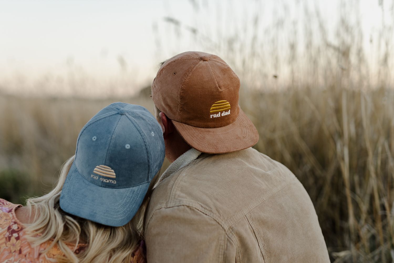 Two people in baseball caps sharing a tender moment in a field during golden hour.