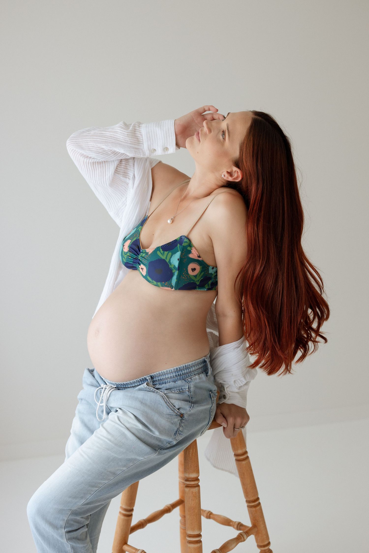 Artistic maternity photo with woman in white shirt and jeans against light background.