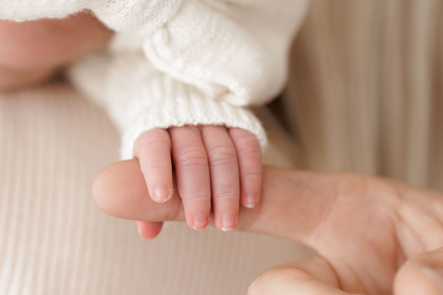 Close-up of tiny baby hand grasping adult finger in tender moment.