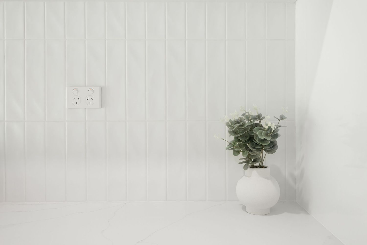 A minimalist white room features a small potted plant on a windowsill with soft natural light streaming in.