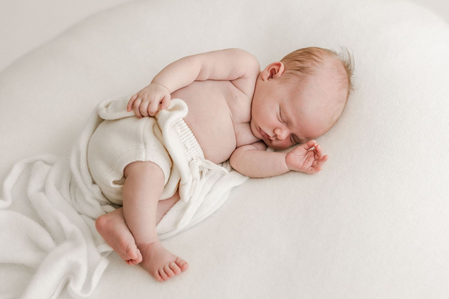Sleeping baby in white onesie lying on light background.