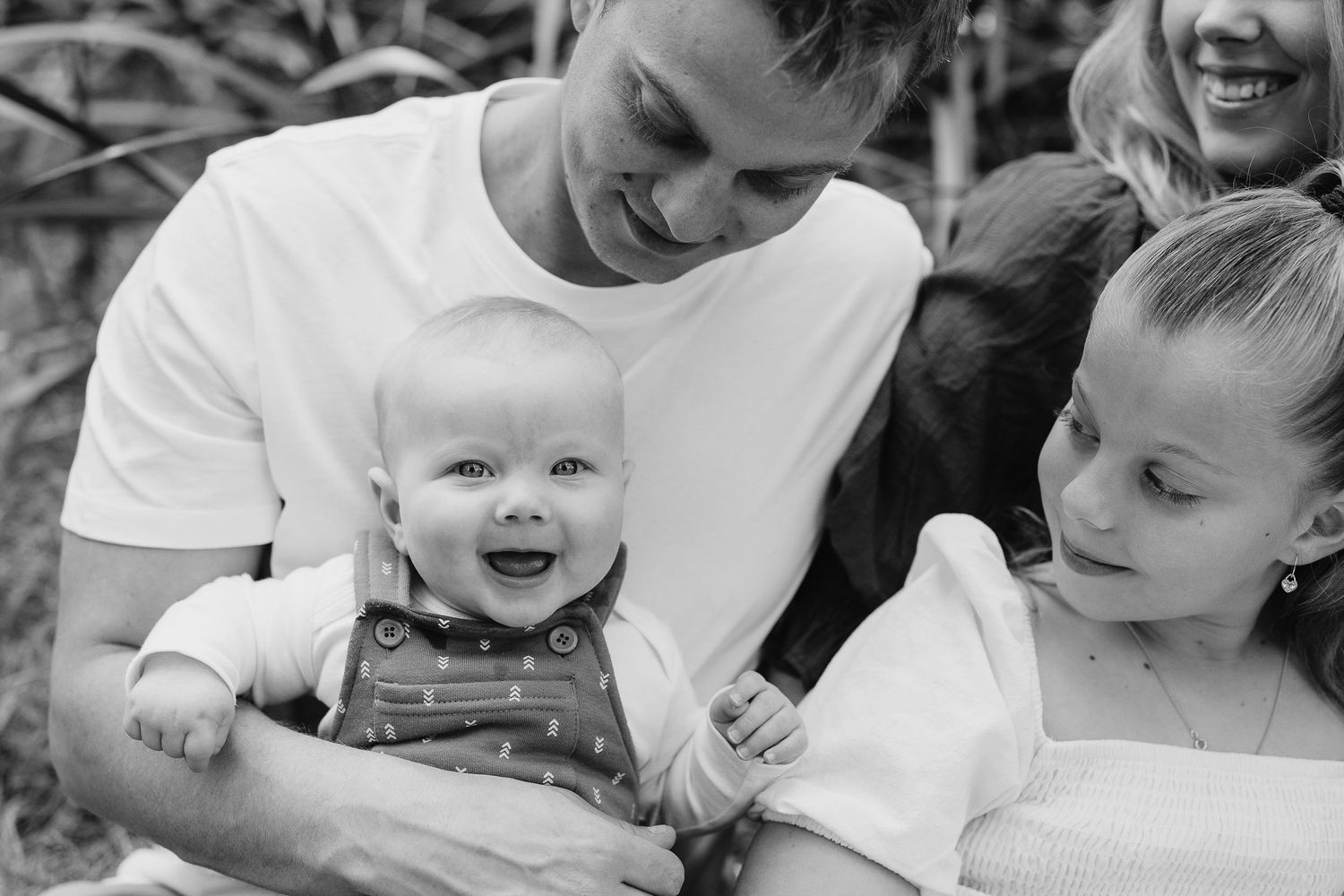 Black and white candid photo of happy toddler and family sharing joyful moment outdoors.