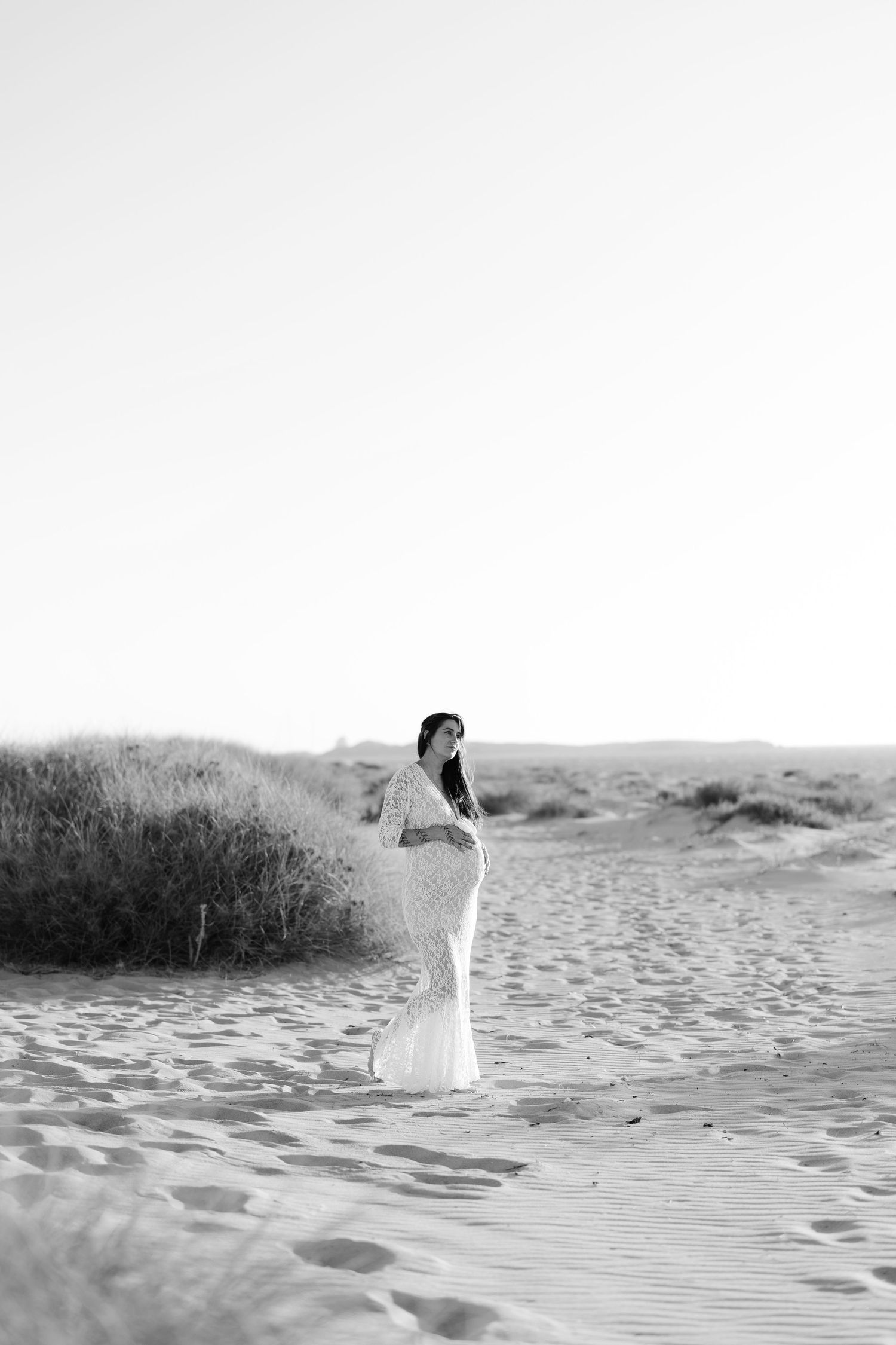A person in a white dress walking along a misty beach shoreline at dusk.