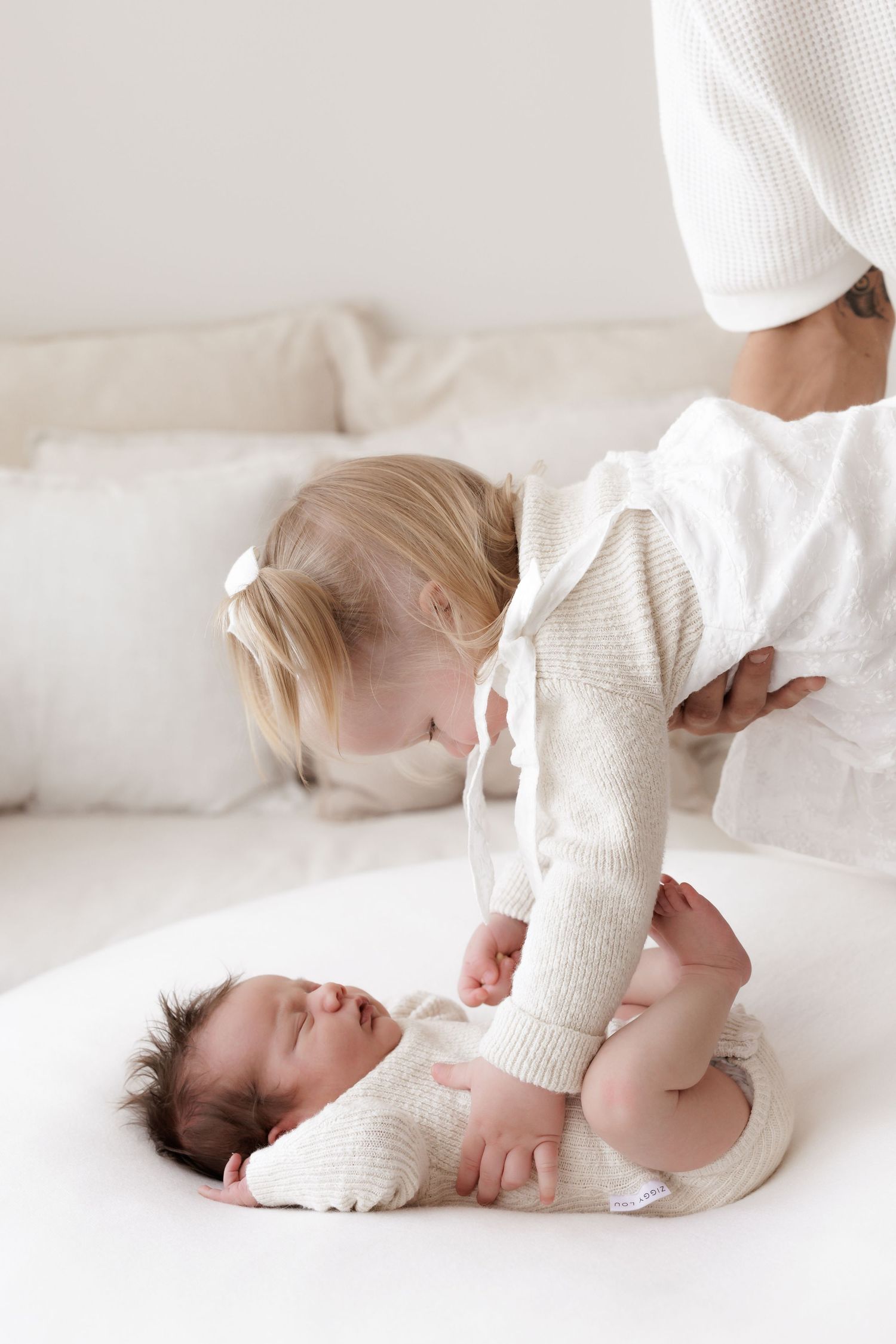 Two small children in white sweaters playing together on light bedding.