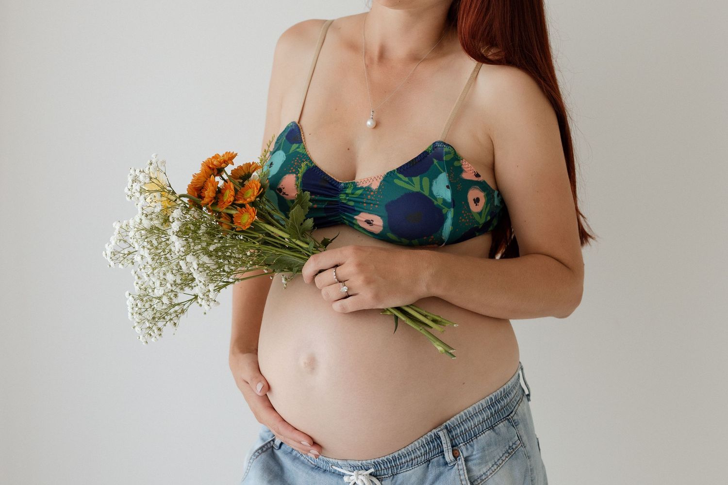 Maternity photo with woman holding orange flowers against white backdrop.