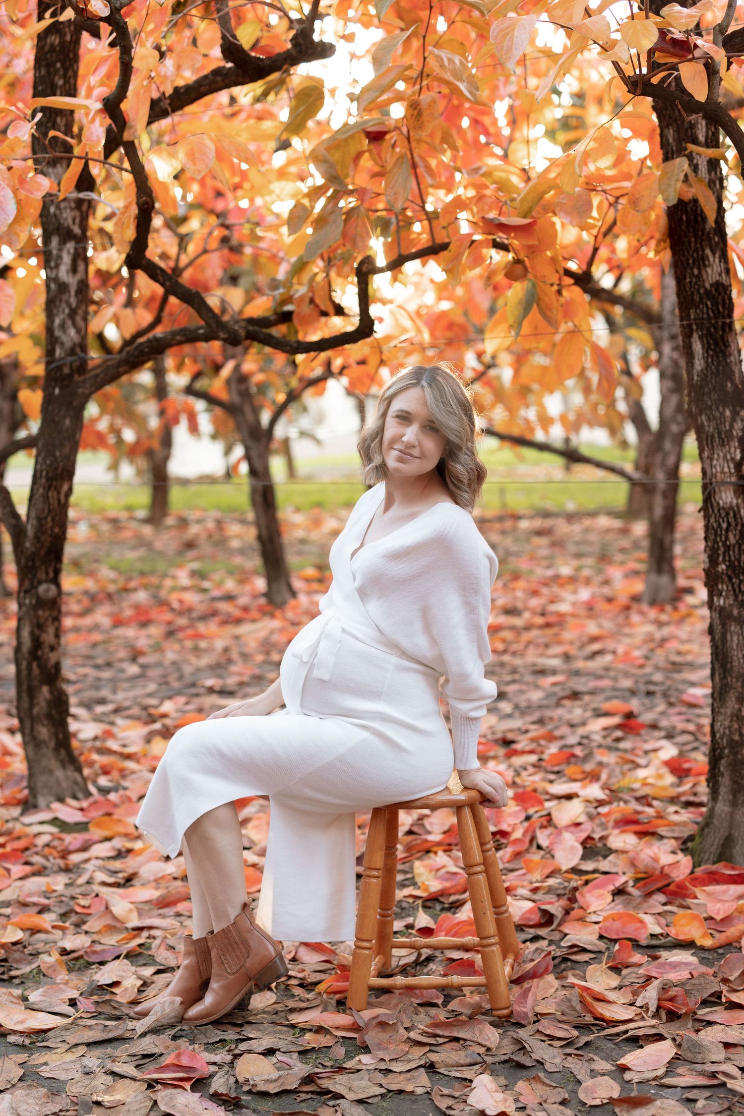 A maternity photo in autumn featuring a white dress against vibrant orange fall foliage.