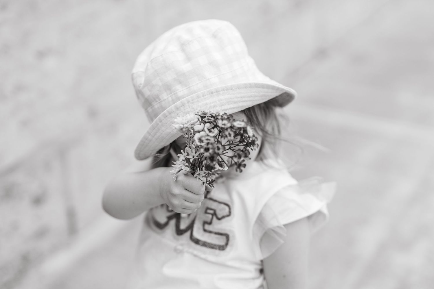 Black and white close-up of someone holding wildflowers while wearing a bucket hat.