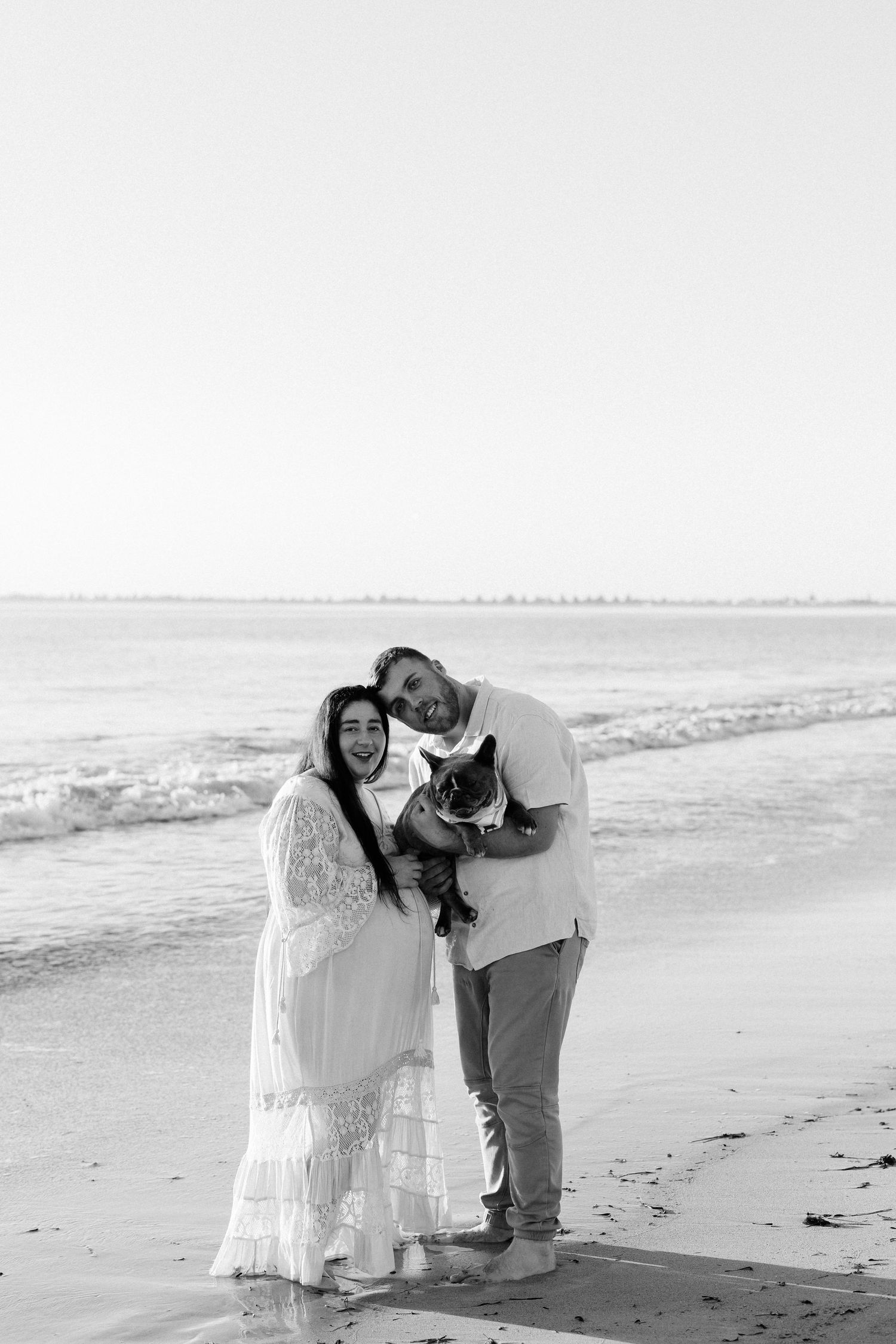A couple shares an intimate moment on the beach in black and white photography.
