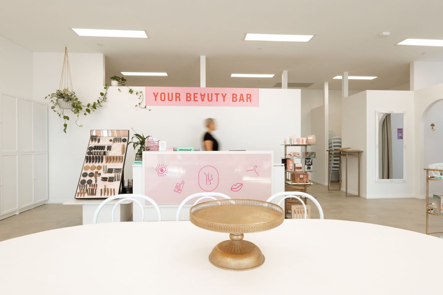 A bright, modern beauty salon interior with white walls, clean lines, and a minimalist retail display area.