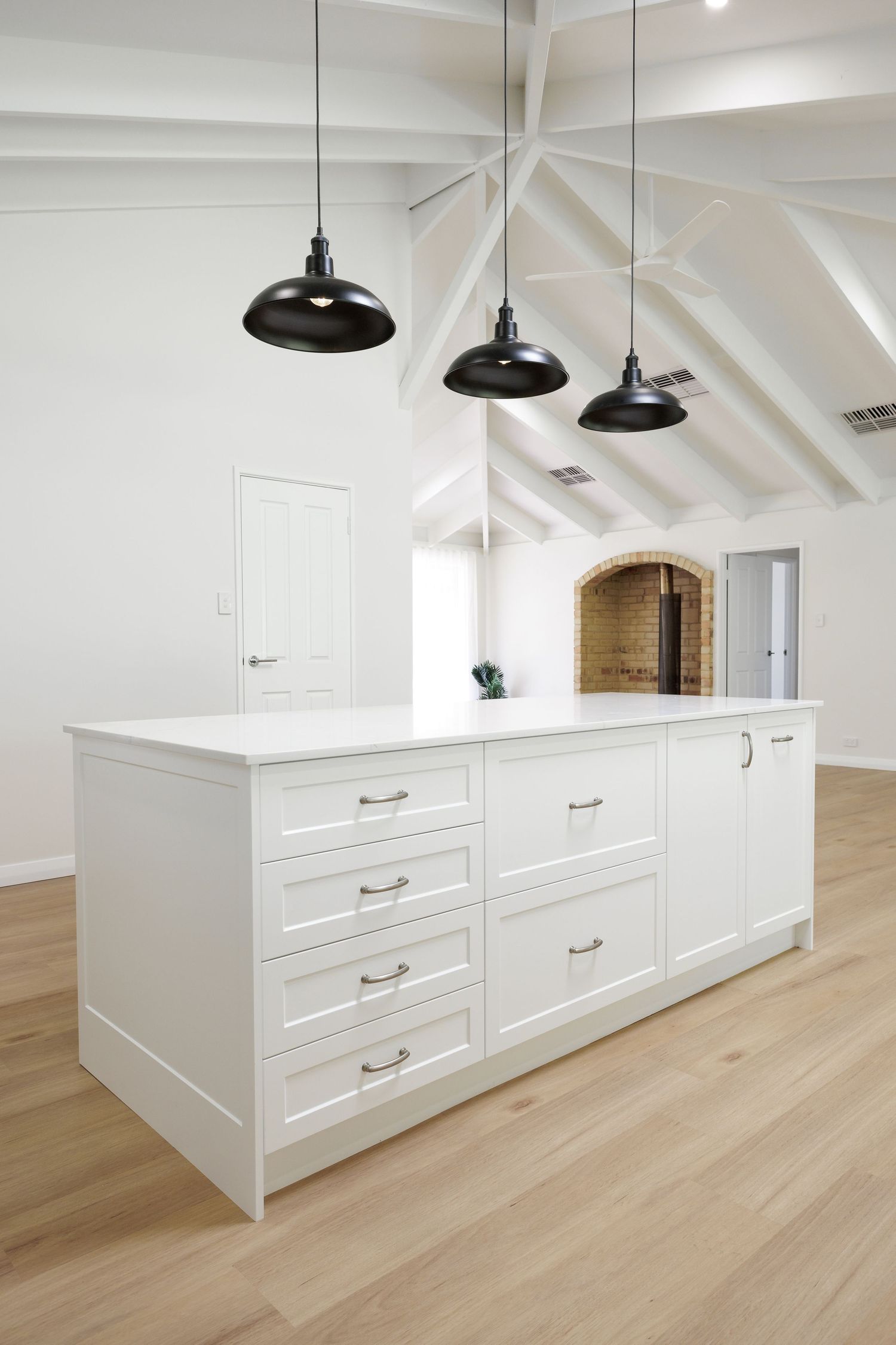 Modern white built-in storage cabinets with drawers and pendant lights in a bright room with light hardwood flooring.