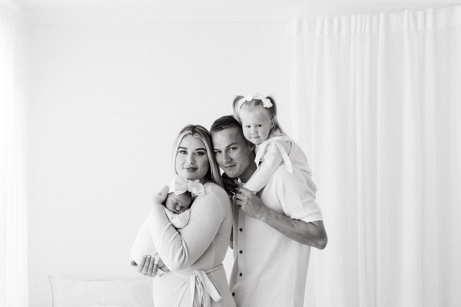 A family in white outfits poses together against a bright backdrop for a portrait.