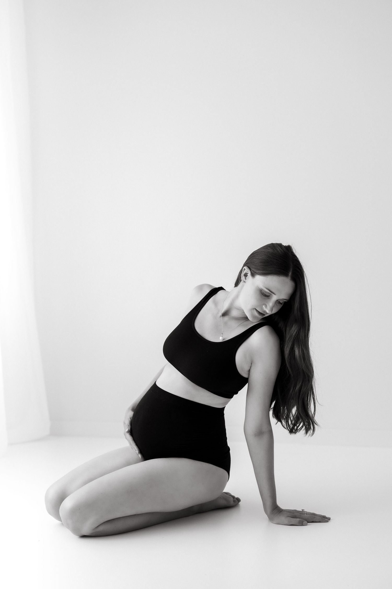Black and white artistic maternity pose on white seamless background.