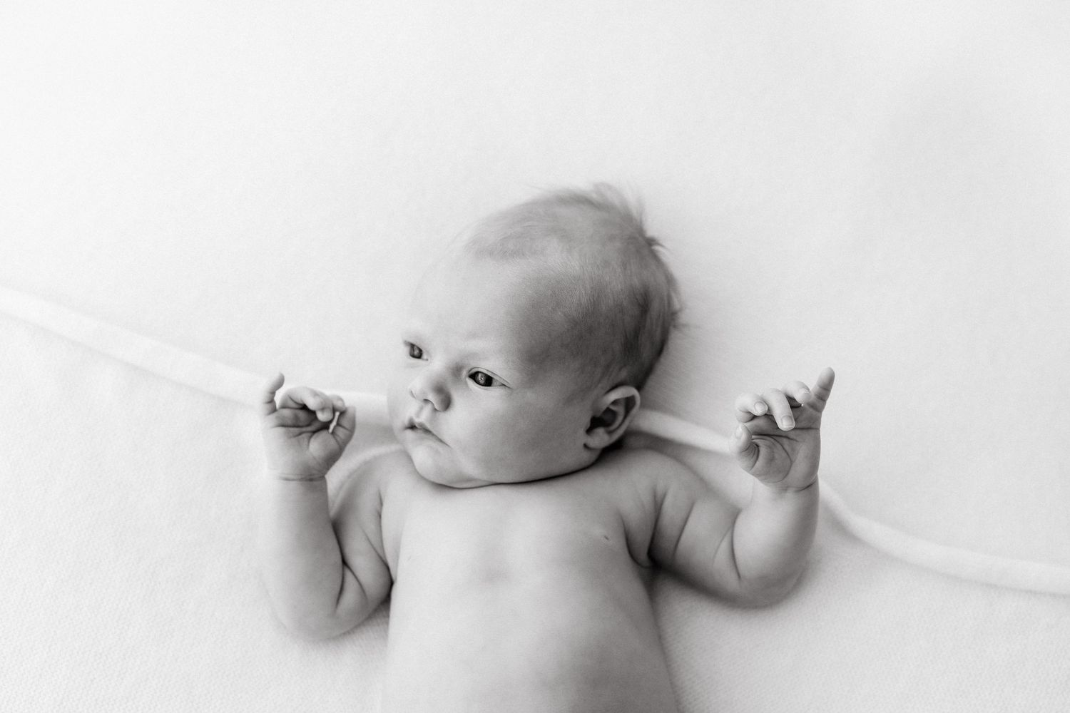 Black and white photo of newborn baby lying on white background with arms spread.