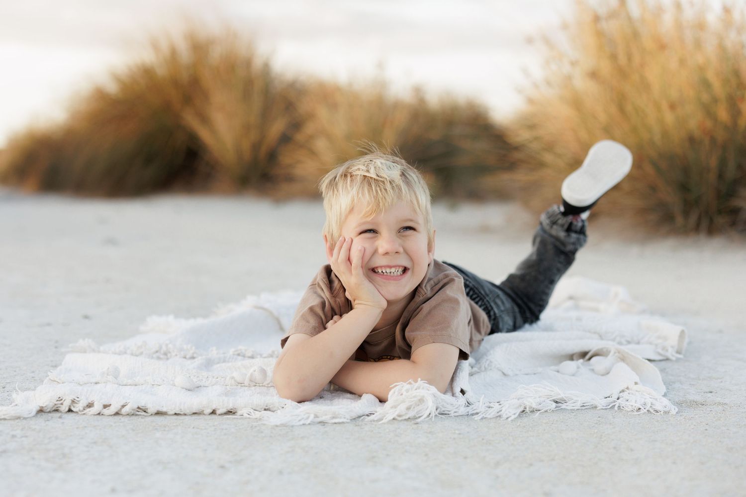 A child lying on a blanket outdoors poses with a bright smile.