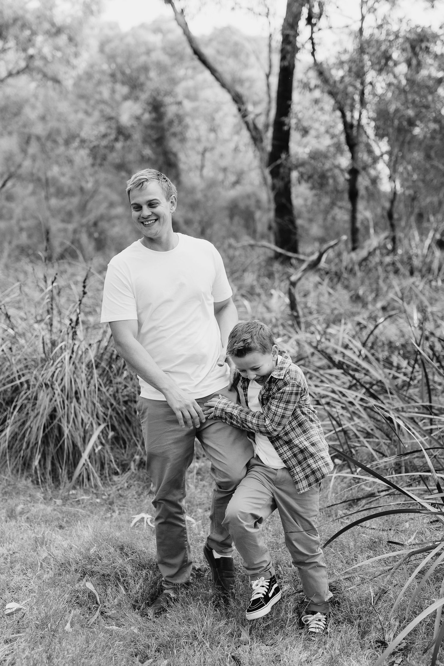 Black and white photo of two people playing in tall grass outdoors.