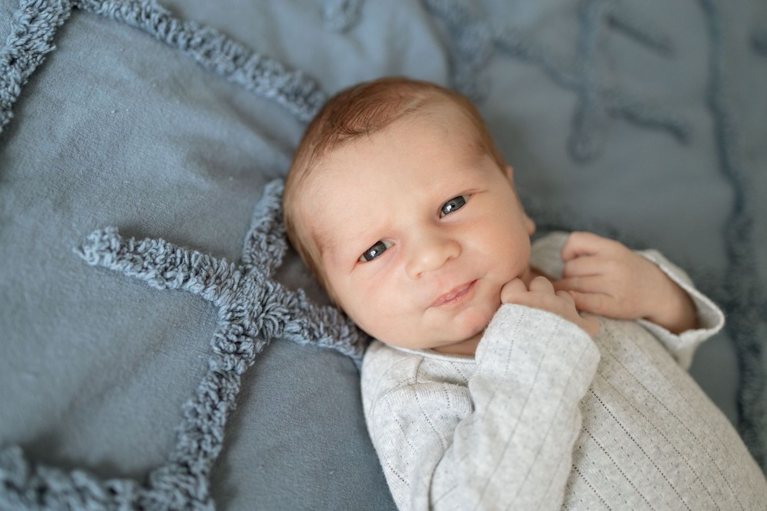 A baby in white knit clothing rests on a gray textured blanket.