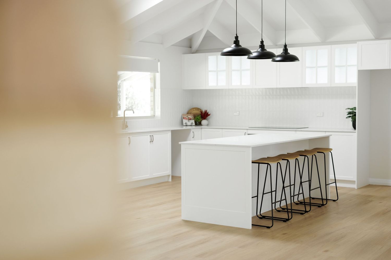 Bright modern kitchen interior with white walls, wood floors, and pendant lighting over a breakfast bar.