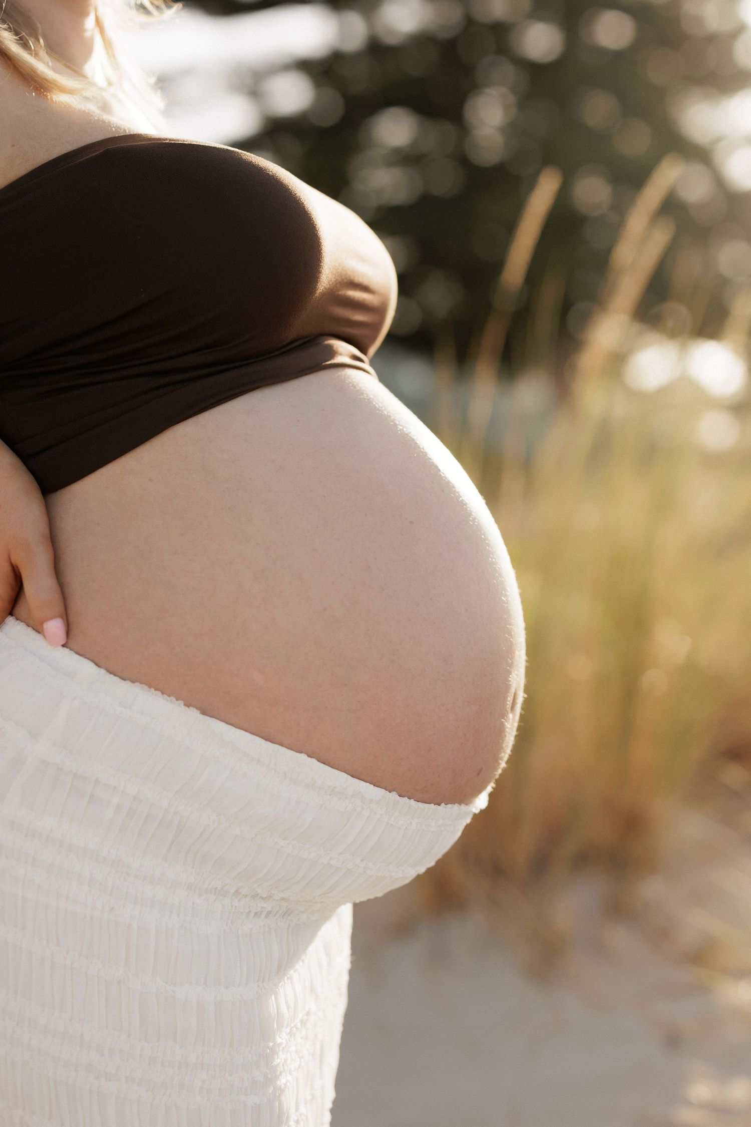 Side view of pregnant belly silhouetted against sunset light.