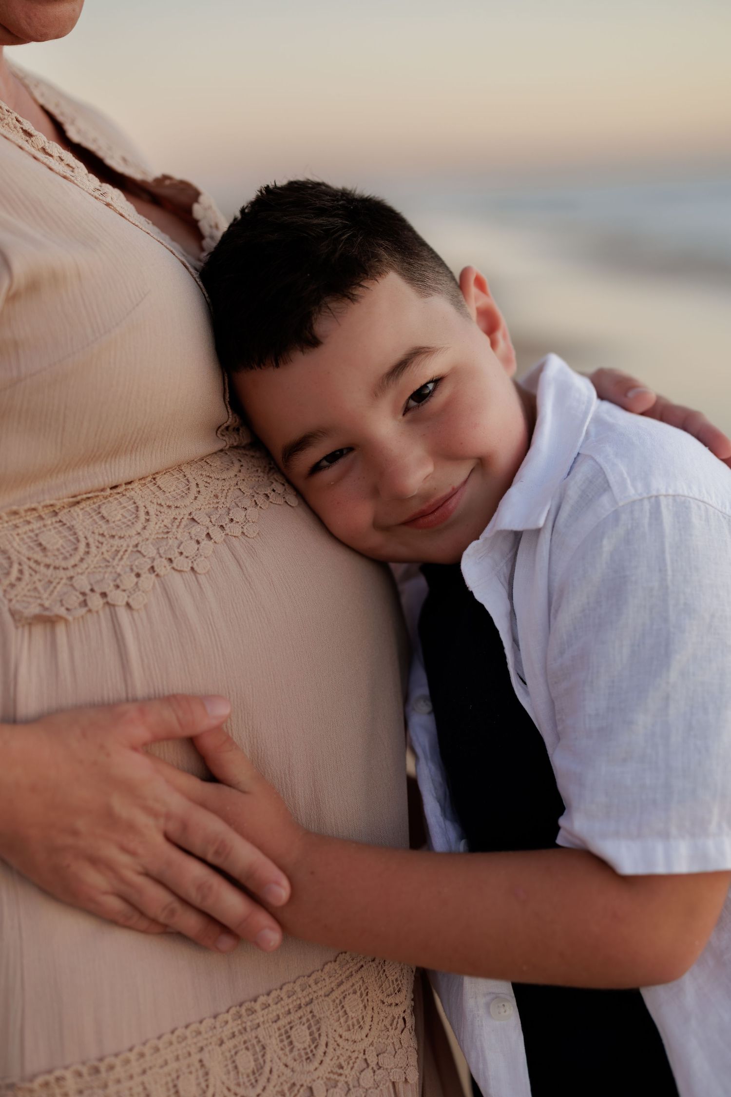 A child in a white shirt hugs a pregnant belly with love and tenderness.