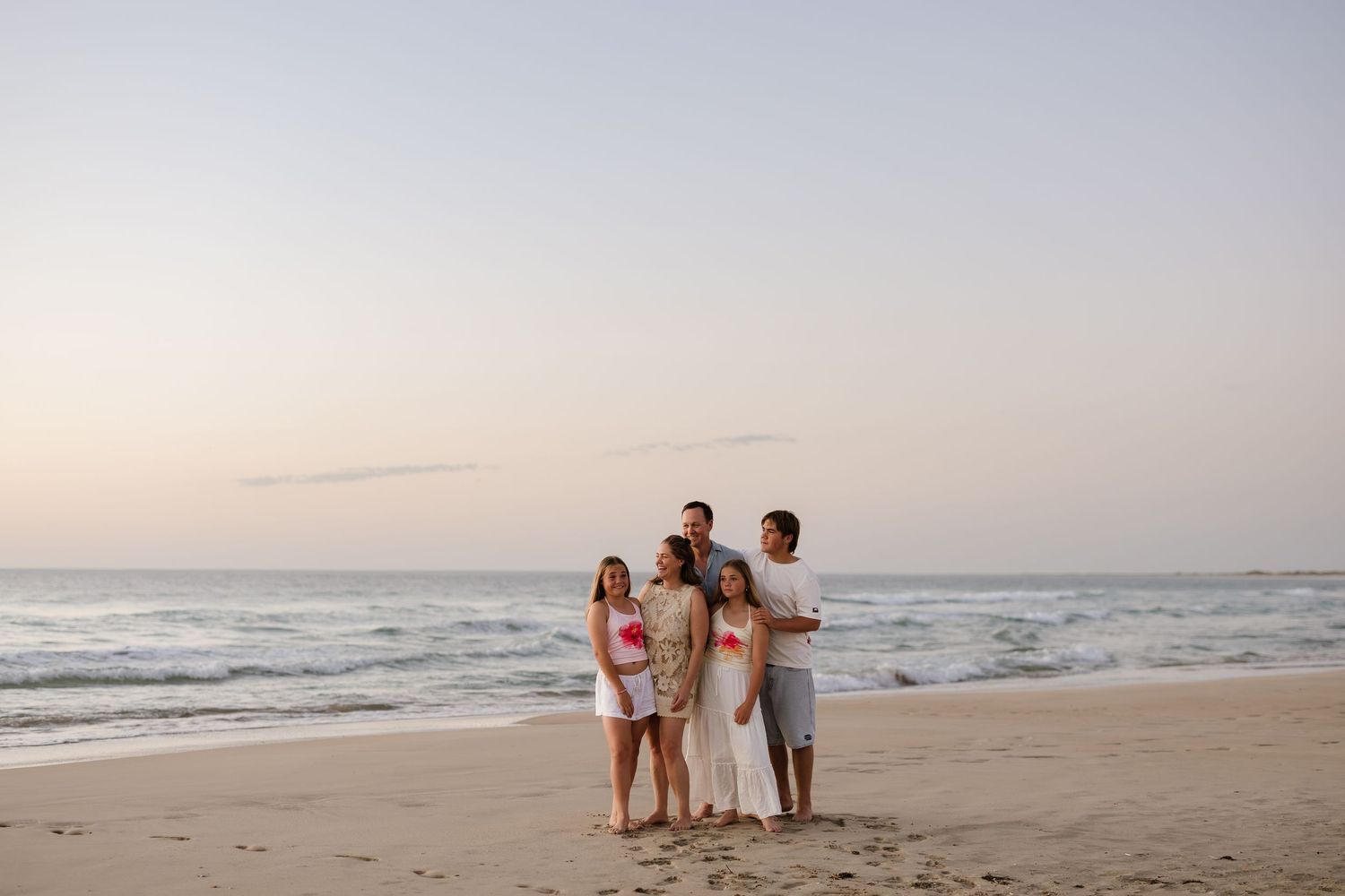 A family stands together on a beach at sunset with the ocean waves rolling in behind them.
