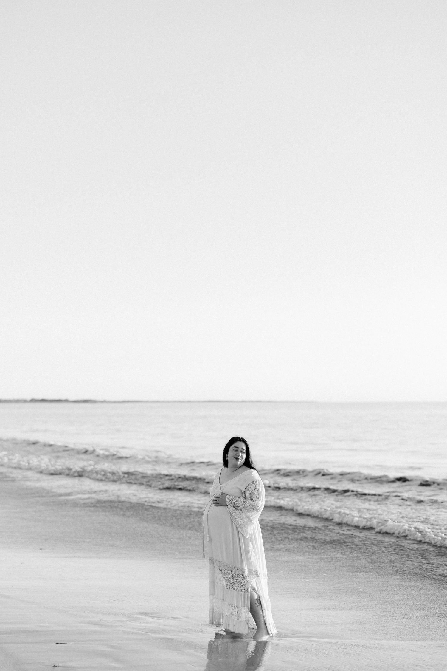 A figure in white stands along the shoreline during an overcast beach day.