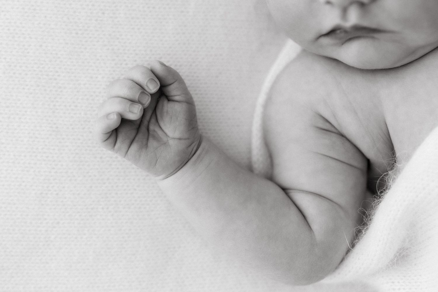 Close-up of infant's tiny fist and arm resting on white fabric.