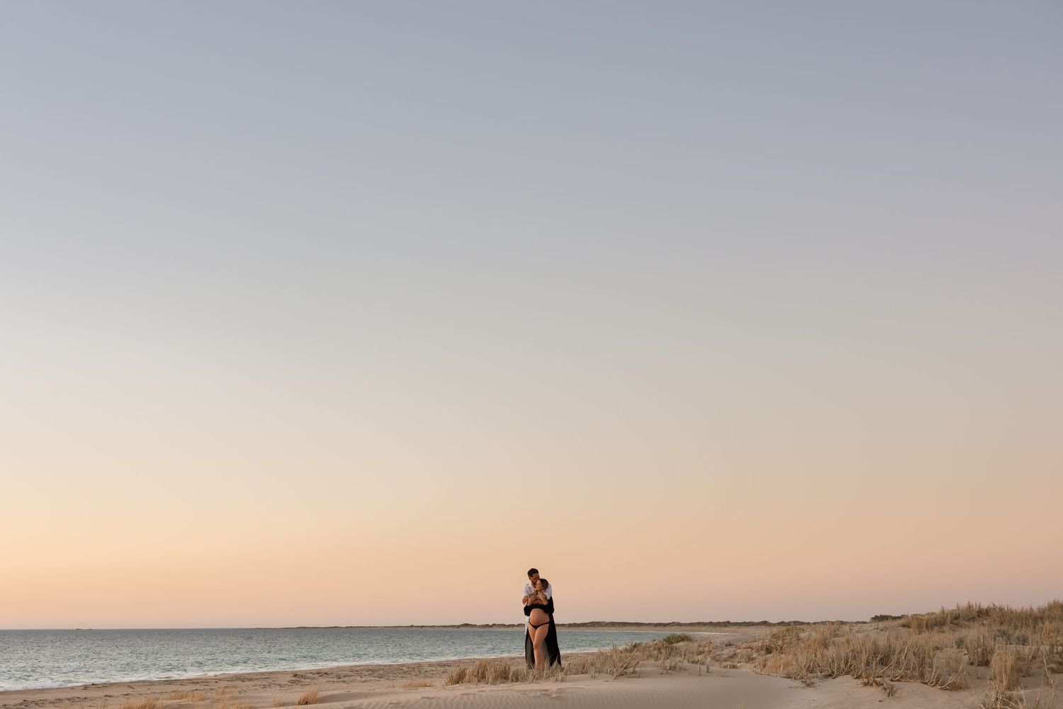 Distant silhouettes standing together on beach shoreline at sunset.