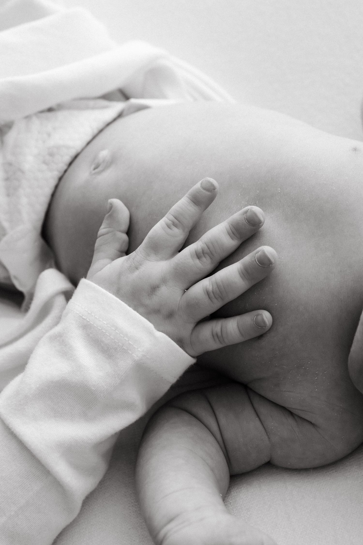 Black and white close-up of baby's small hand resting on soft fabric.