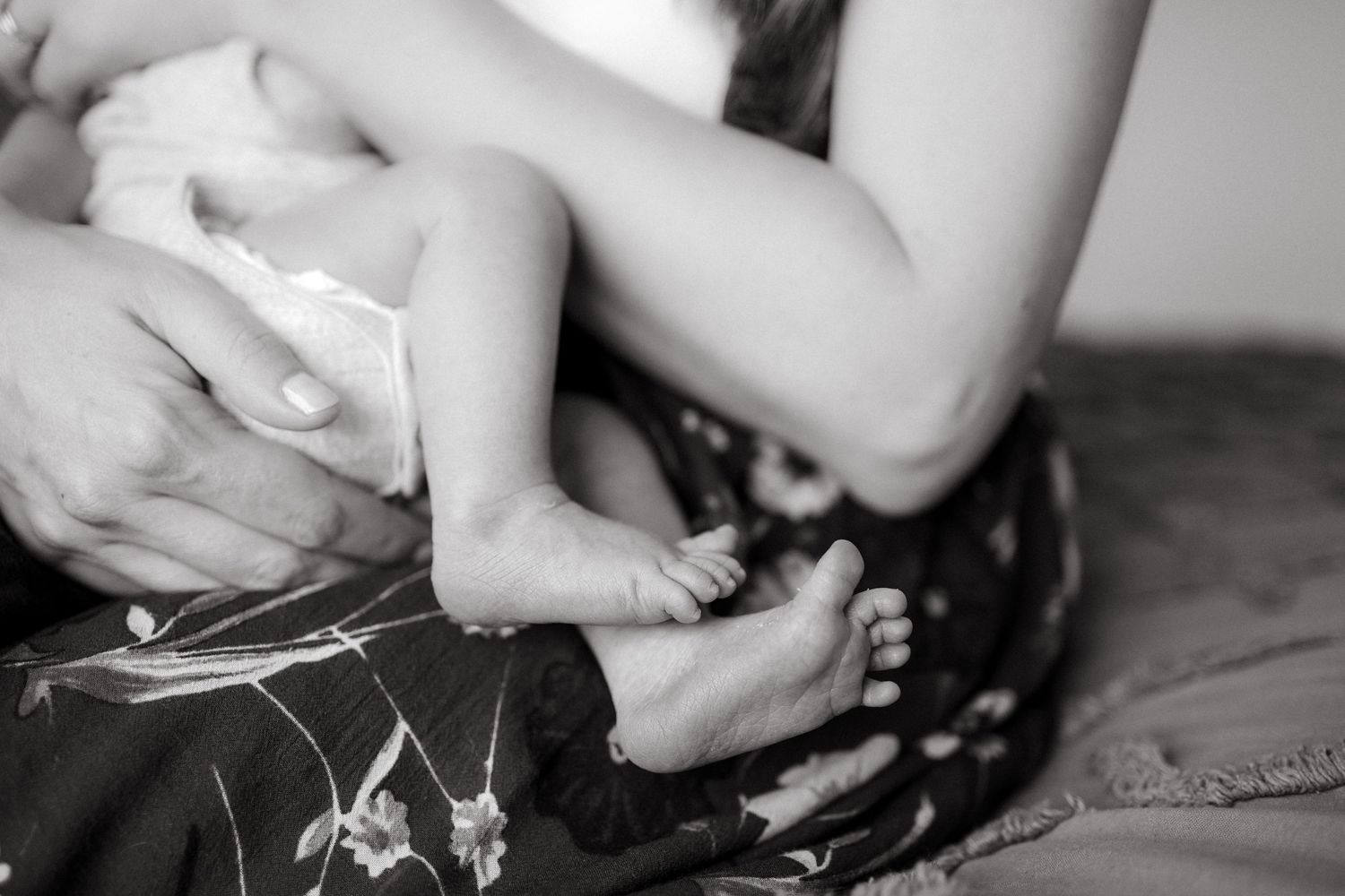 Black and white close-up of tiny baby feet being gently held against floral fabric.